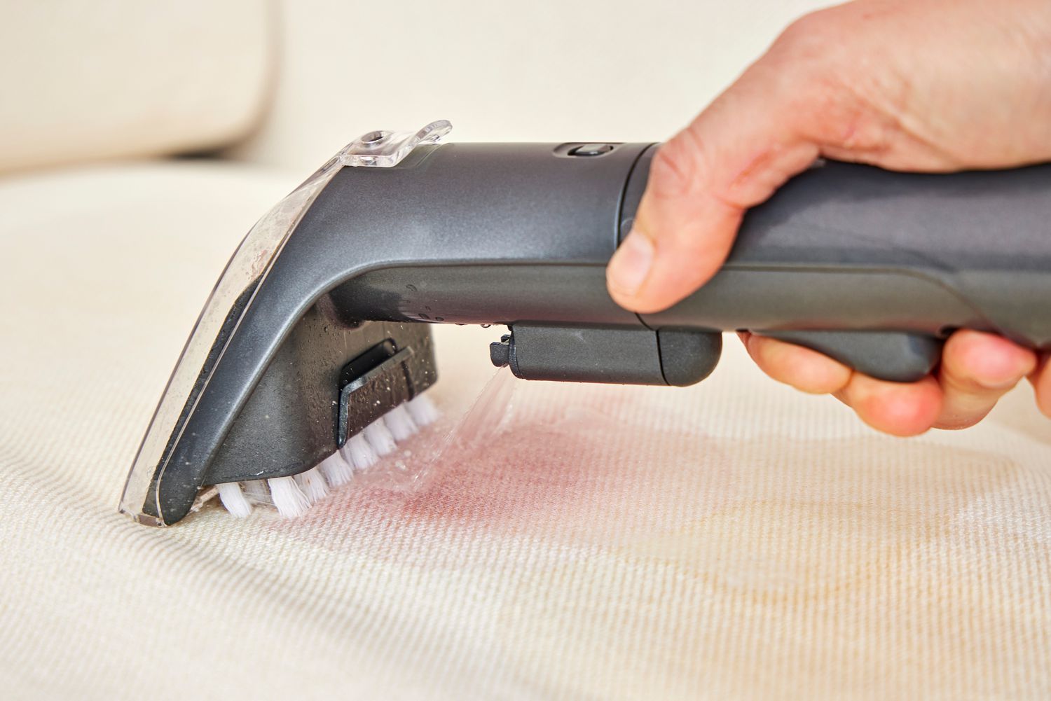 A person uses the Bissell Little Green Cordless Portable Carpet Cleaner 3682 to clean white fabric