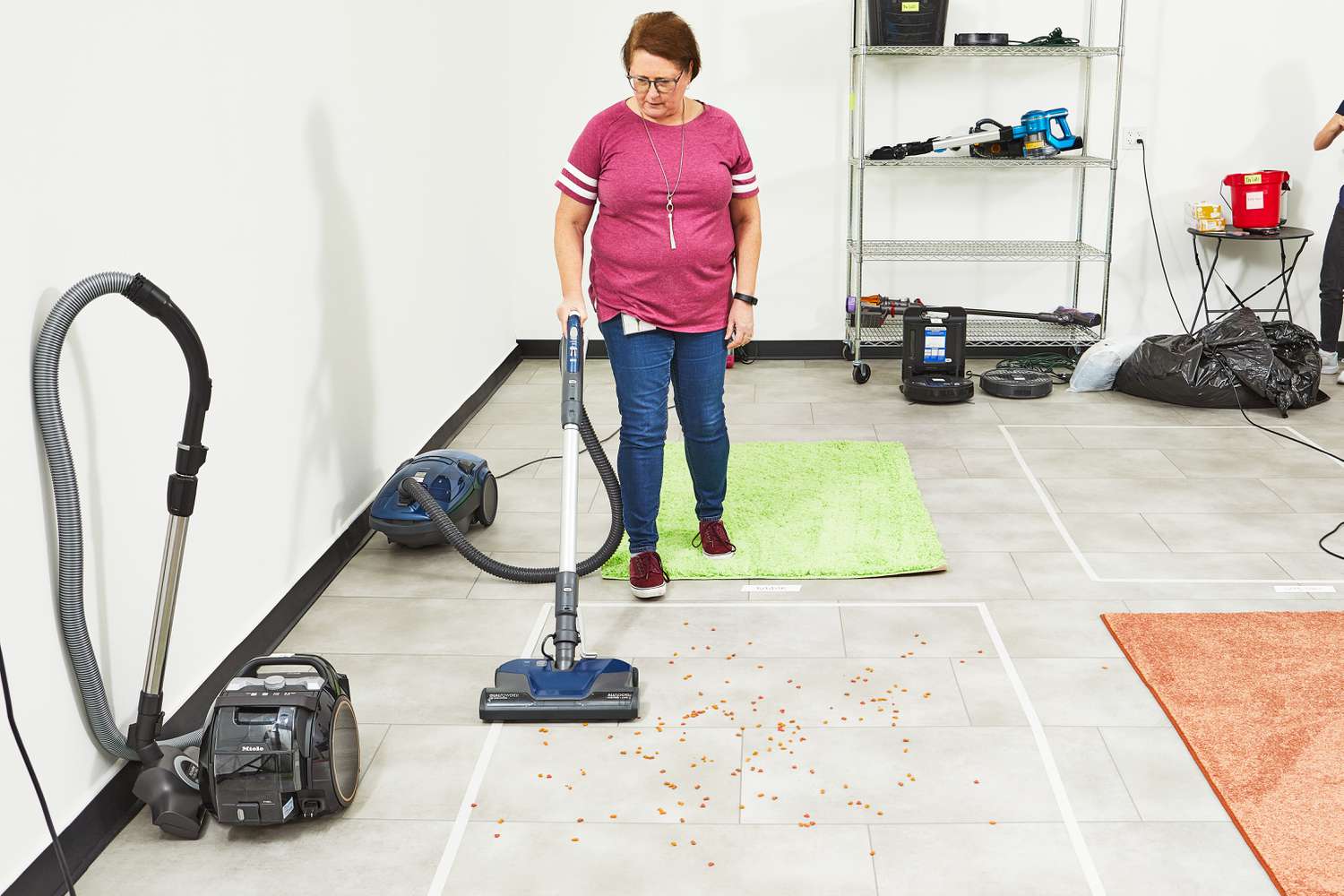 Person using a Kenmore Pet-Friendly POP-N-GO Bagged Canister Vacuum to sweep up pet food on white tiled flooring