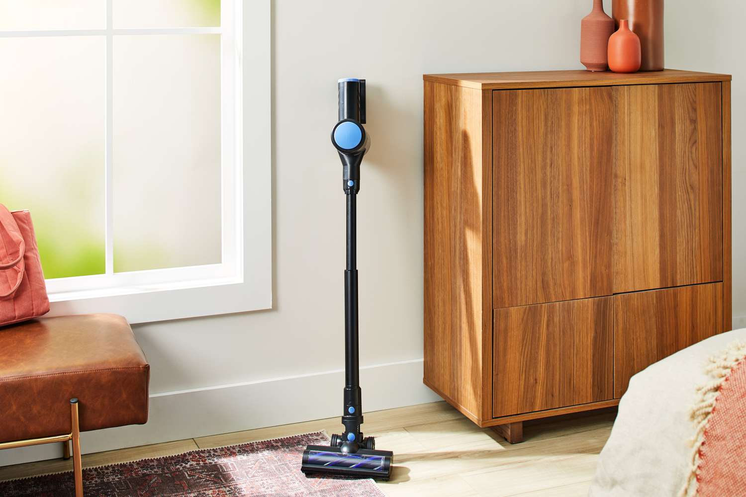 The WOWGO Cordless Vacuum Cleaner leaning against a wall next to a cabinet and leather bench.