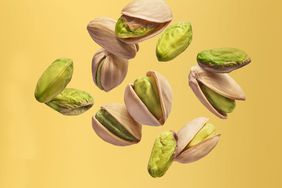 Fresh, raw, whole, and cracked pistachios thrown in the air, set against a yellow background.