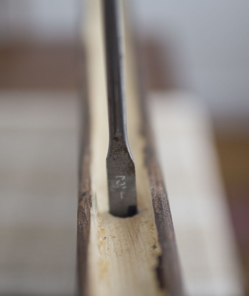 Drill bit entering pine wood shelf