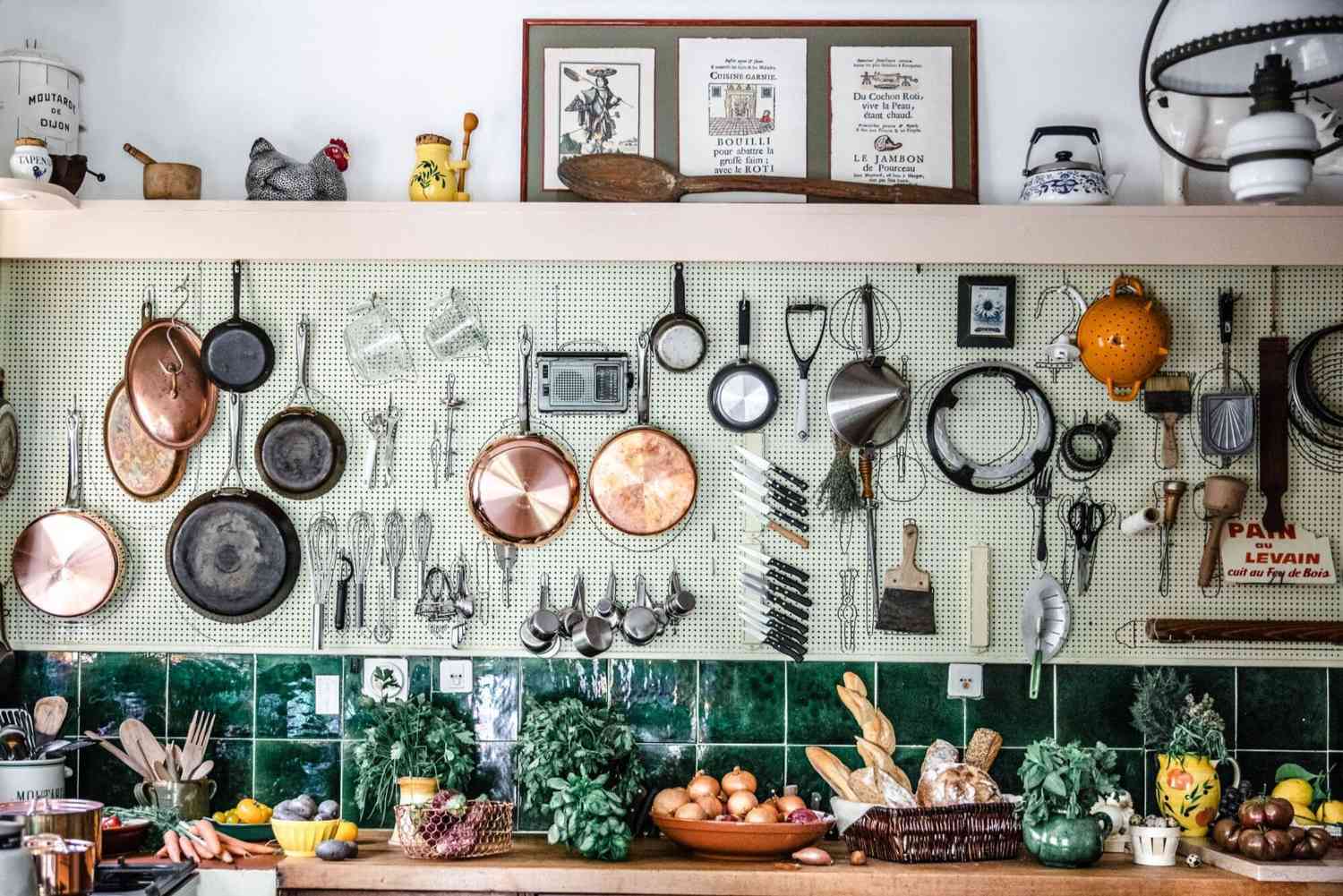 Julia Child's famous kitchen peg board filled with pots, tools, utensils, pans, and a bevy of produce on the counter below