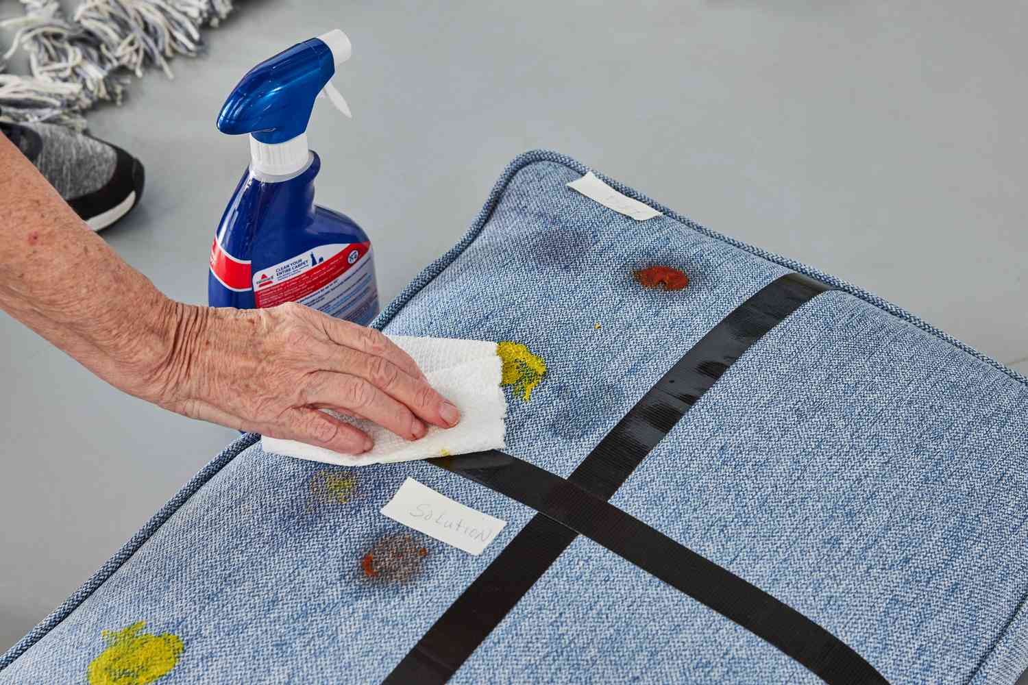 A person uses Bissell Advanced Oxy Stain Pretreat to clean food stains off a couch cushion.