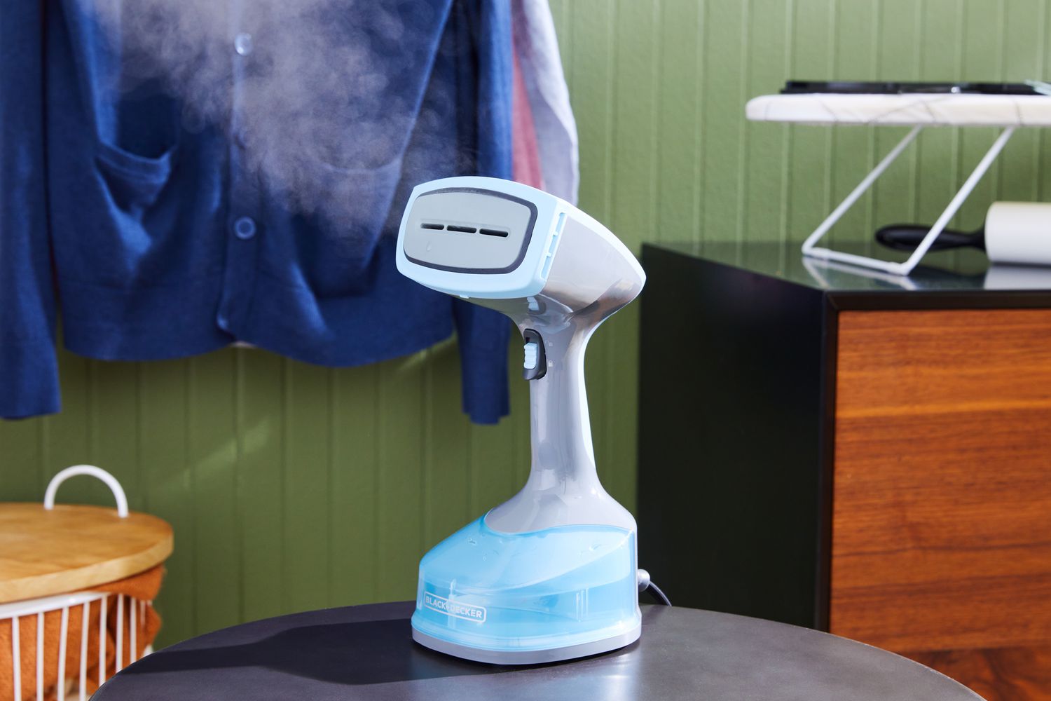 The BLACK+DECKER HGS200 Advanced Handheld Steamer with steam coming out and clothes handing in the background. 