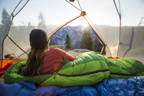 A woman taking in the view of Half Dome from insider her tent while camping in the mountains.