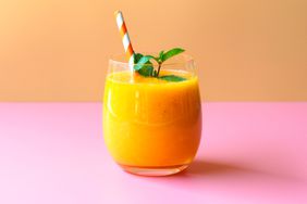 Mango smoothies topping with mint leaf on orange and pink background for summer fruit drink concept.