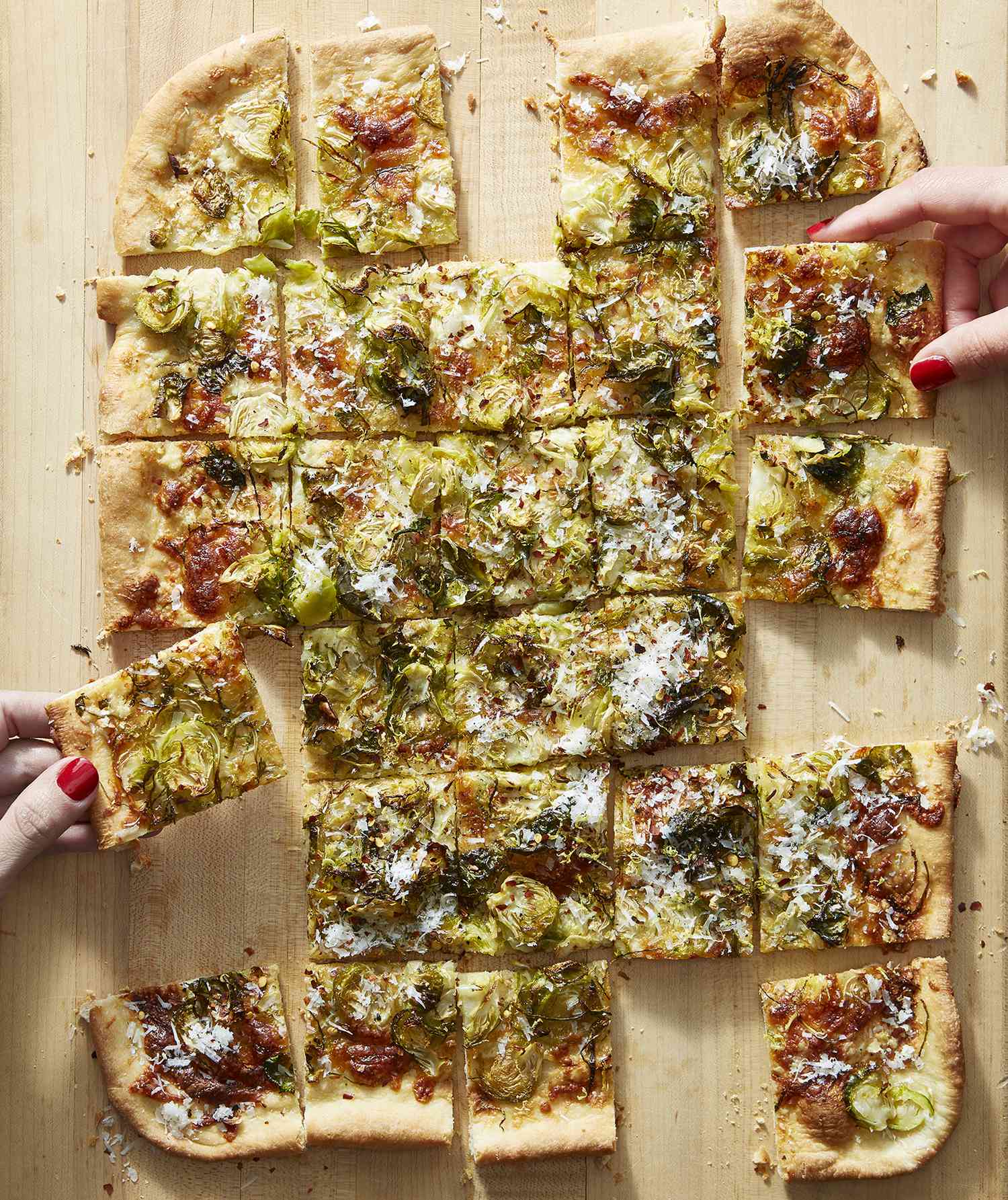 Overhead View of Brussels Sprouts Flatbread Cut into Pieces with Hands Grabbing Slices