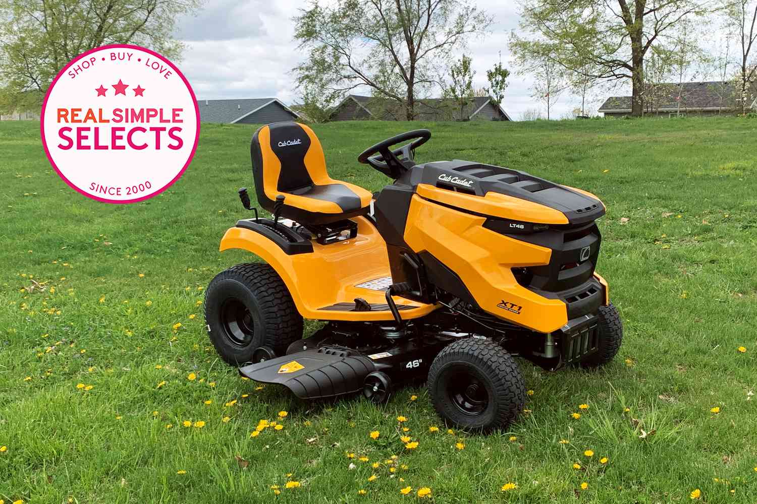 A yellow riding lawn mower on grass with roofs in the background