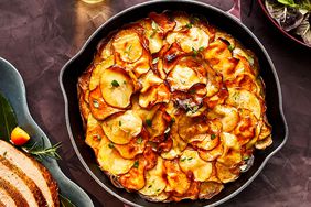 Garlicky Herb-Butter Layered Potatoes served in a cast iron dish and displayed on a table with other holiday dishes.