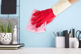 A person cleans a painted wall with a pink cloth while wearing a red cleaning glove