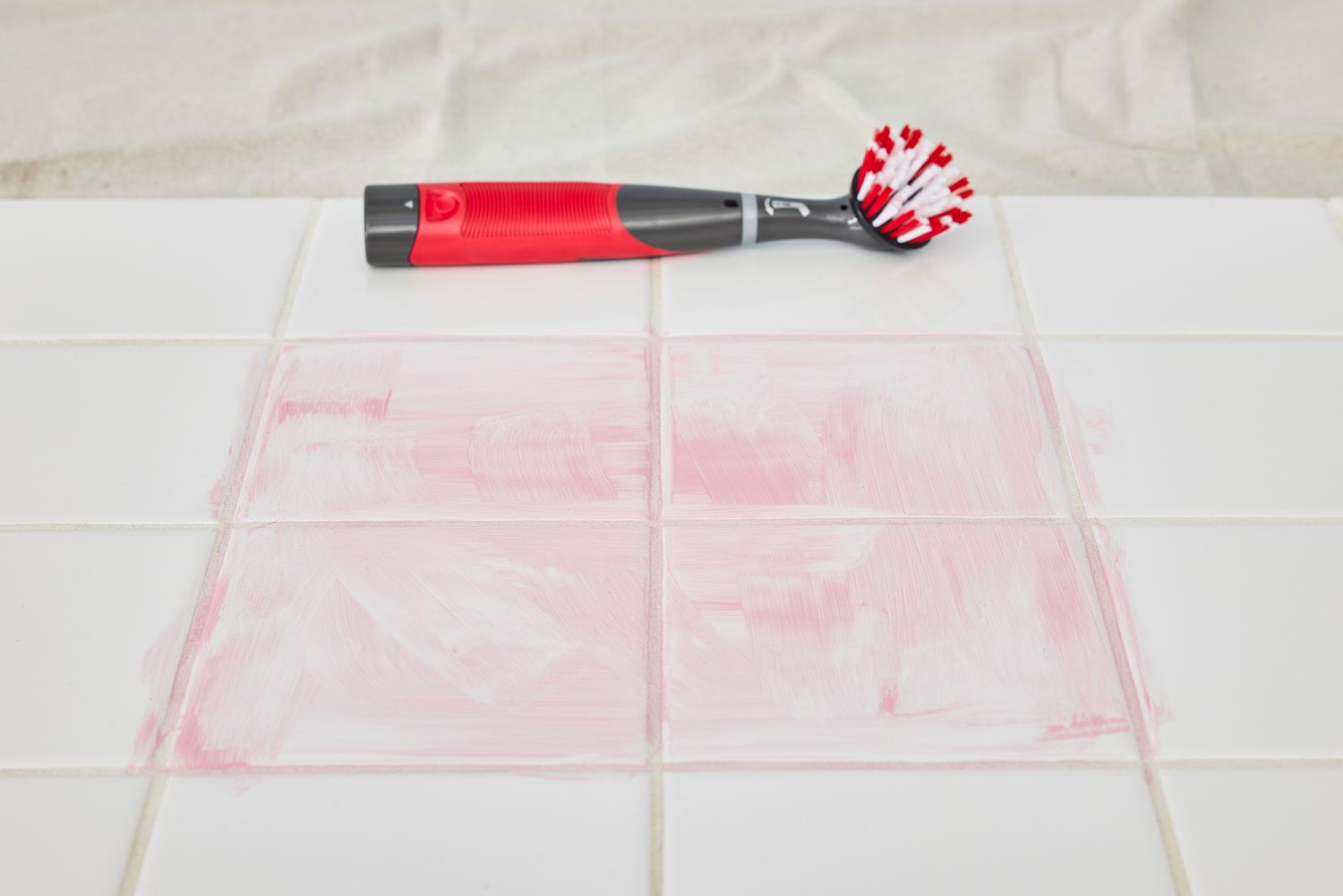 Rubbermaid Reveal Power Scrubber placed on white floor tile next to four sections of pink cleaning product smudge