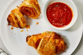 Pepperoni pizza croissants are served up on a white plate with a side of marinara dipping sauce.