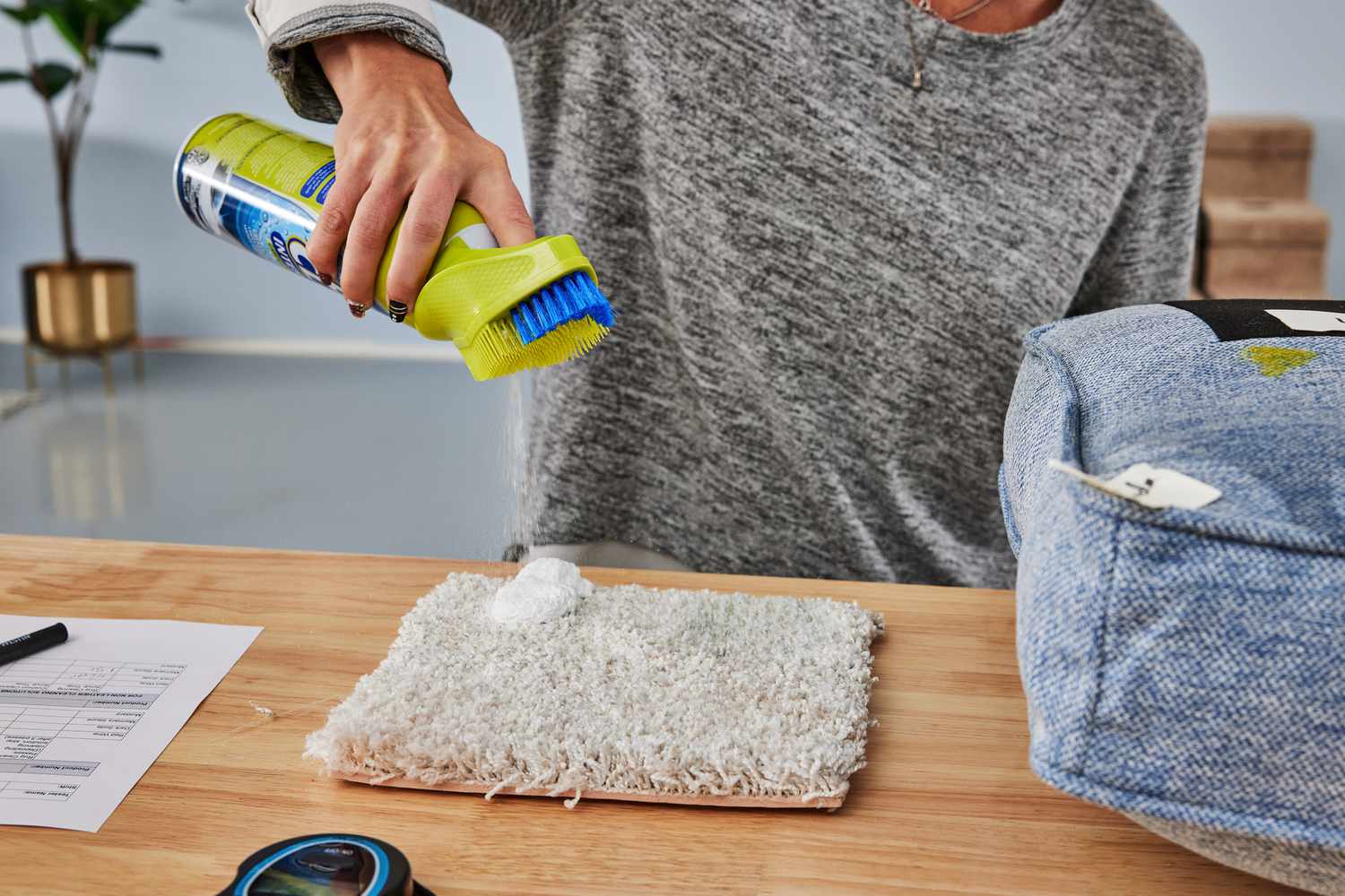 person spraying OxiClean Total Interior Carpet & Upholstery Cleaner onto piece of carpet