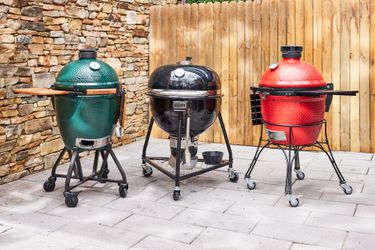 Three kamado grills on a stone patio