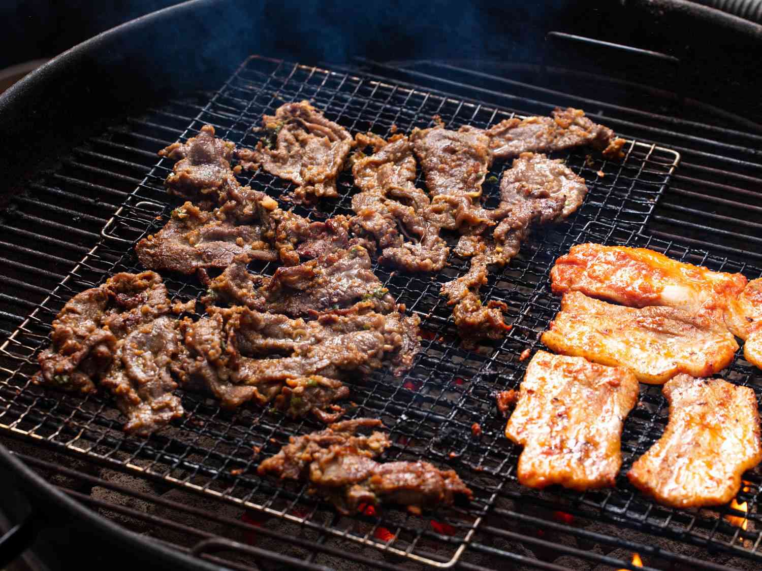 Beef bulgogi and pork belly cooking on a charcoal grill.