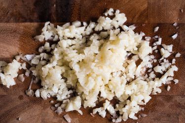 Closeup of finely chopped garlic on a wooden cutting board.