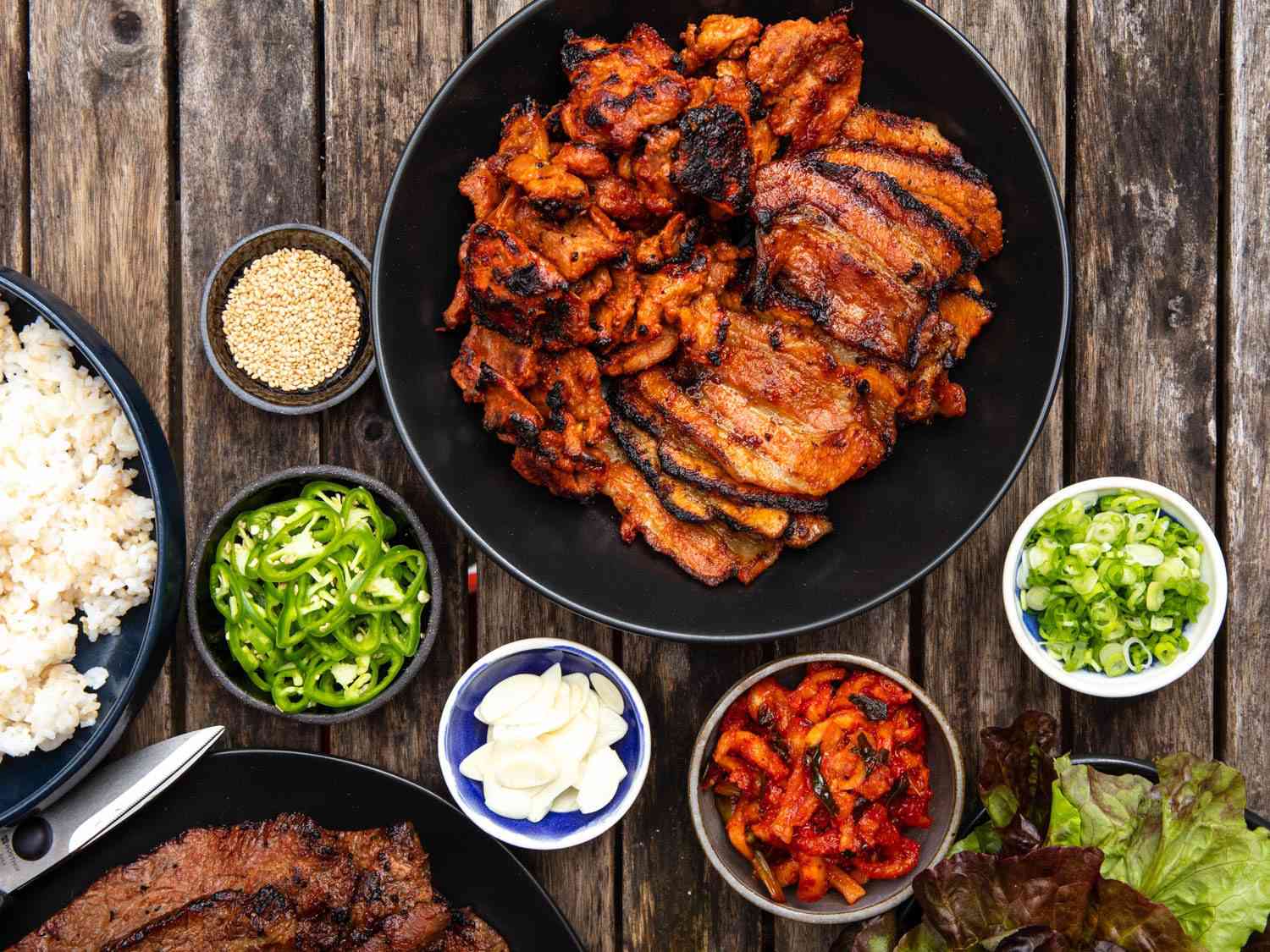 Overhead shot of a serving platter of grilled daeji bulgogi surrounded by small dishes of garnishes and banchan.