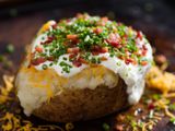 A close up of a split baked potato topped with shredded cheese, sour cream bacon, and chopped chives.