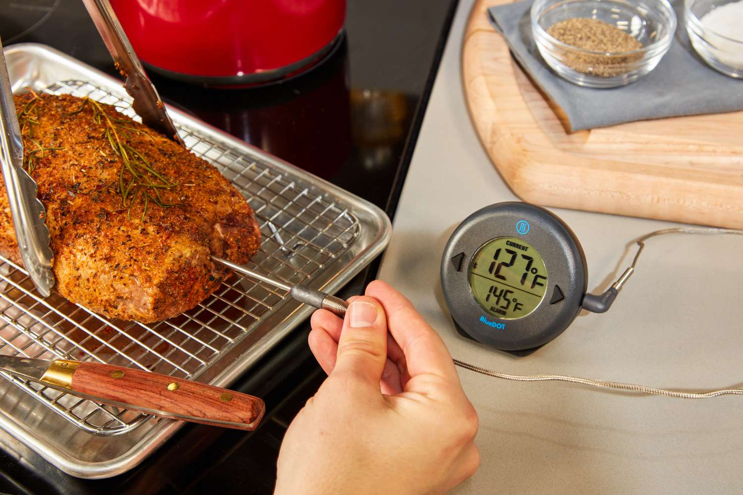 inserting a probe thermometer into a spice rubbed pork tenderloin on a rack