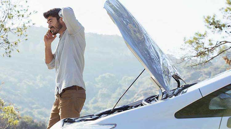 A man talks on his cellphone next to an open car trunk.