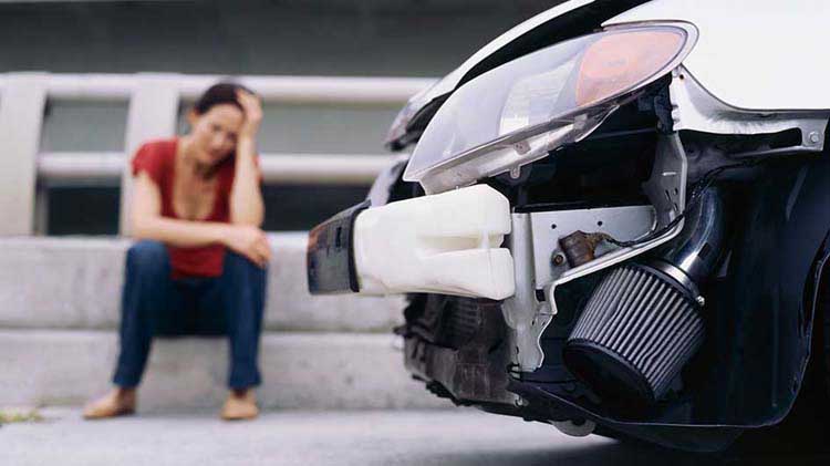 An upset woman sits next to a wrecked car.