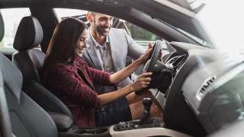 A young lady sits behind the wheel of her car reviewing the dashboard.