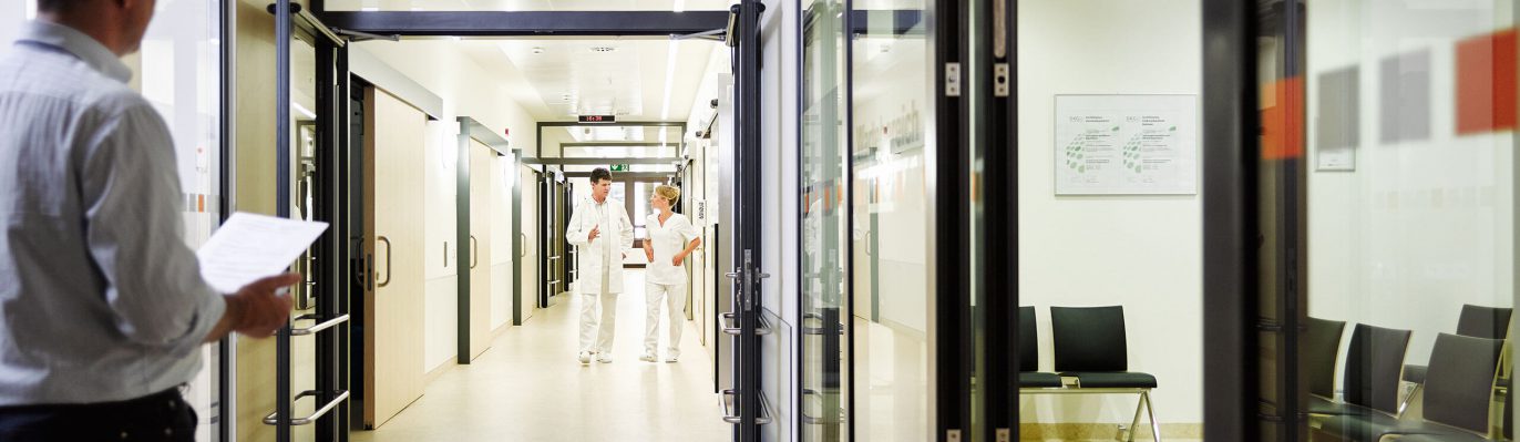 Ärztin und Arzt in Besprechung. Patient füllt Aufnahmebogen aus.