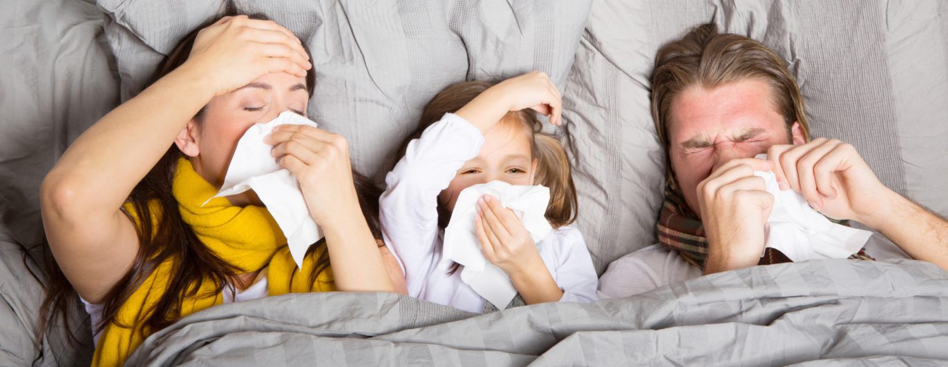 Kranke Familie mit Taschentüchern im Bett.