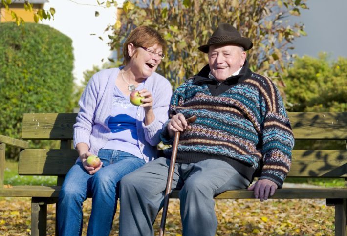 Pflegende Angehörige mit Vater auf einer Bank.