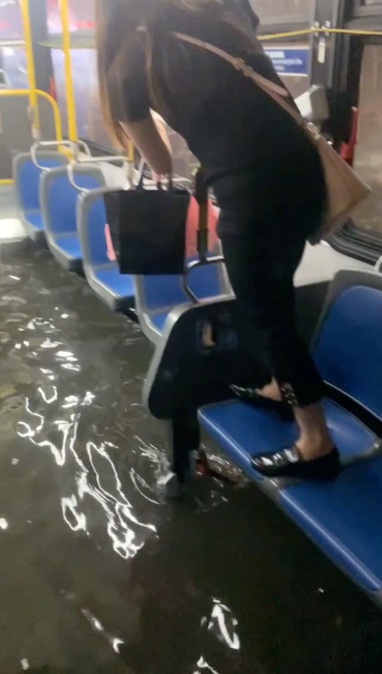 A woman stands on a chair to avoid floodwaters inside an NYC bus