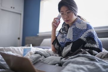 Woman taking temperature in bed with digital thermometer