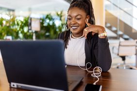 A woman smiling while sitting at a desk in front of an open laptop