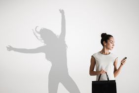 A businesswoman looking at her work phone in front of her own shadow dancing, representing work life balance.