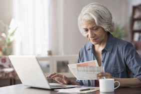 Older woman at a desk entering information from statements into a laptop