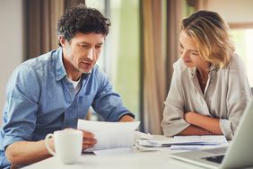 A man and a woman sitting at a dining room table reviewing financial documents