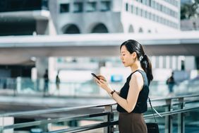 Businesswoman using smartphone on city bridge outside the business building in central business district.