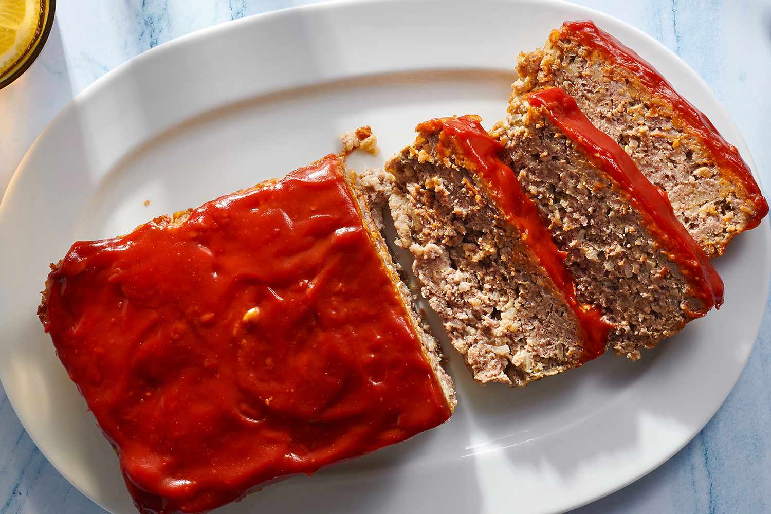 Partially sliced meatloaf with ketchup glaze on a white serving platter