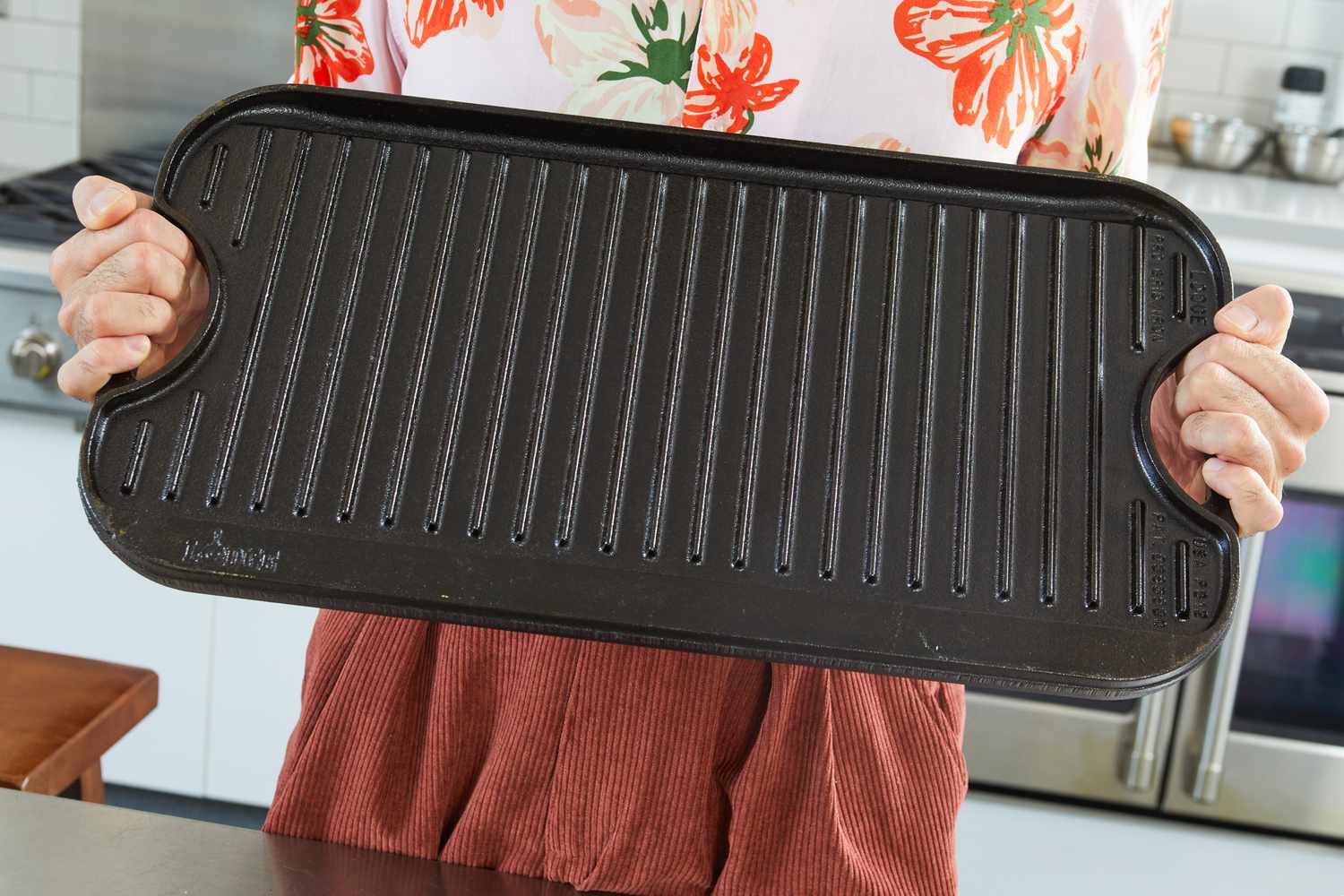 A person holding up the Lodge Cast Iron Reversible Grill/Griddle.