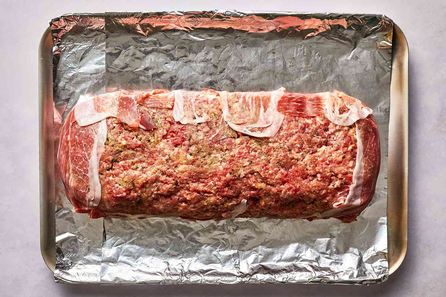 Prosciutto-Wrapped Stuffed Meatloaf on an aluminum foil lined baking sheet 