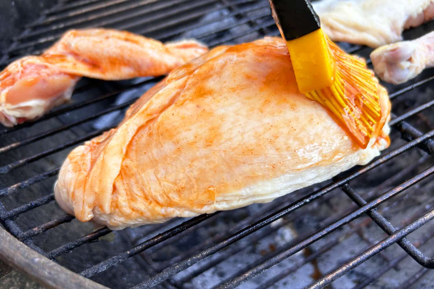 Chicken being brushed with sauce on a grill cooking over FOGO Super Premium Oak Restaurant All-Natural Hardwood Lump Charcoal