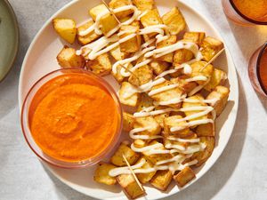 A platter of air fryer patatas bravas, topped with aioli, served with a bowl of romesco sauce