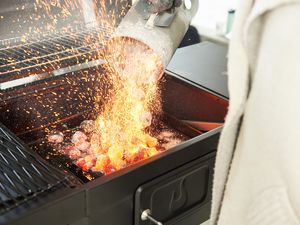 Hand emptying the Weber 7416 Rapidfire Chimney Starter on to a grill 