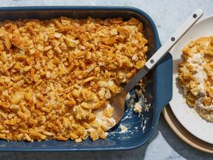 A ritzy chicken casserole with a large serving spoon and portion removed, with a plated portion