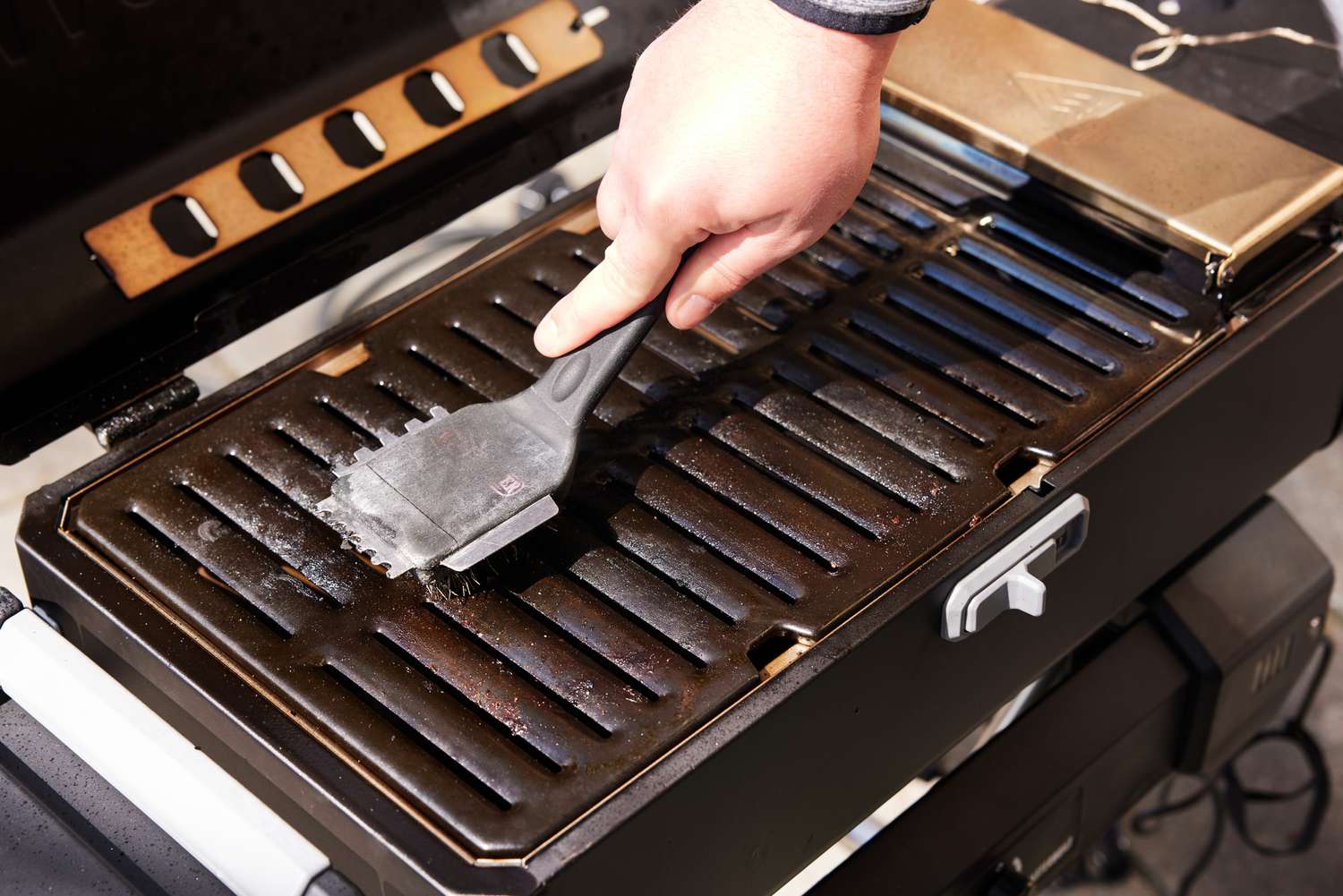 Closeup of a hand cleaning the Masterbuilt Portable Charcoal Grill and Smoker with Cart with a brush 