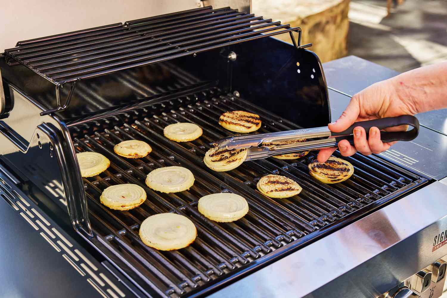 Hand flipping onions with tongs on the Char-Broil Signature Series Amplifire 2-Burner Gas Grill