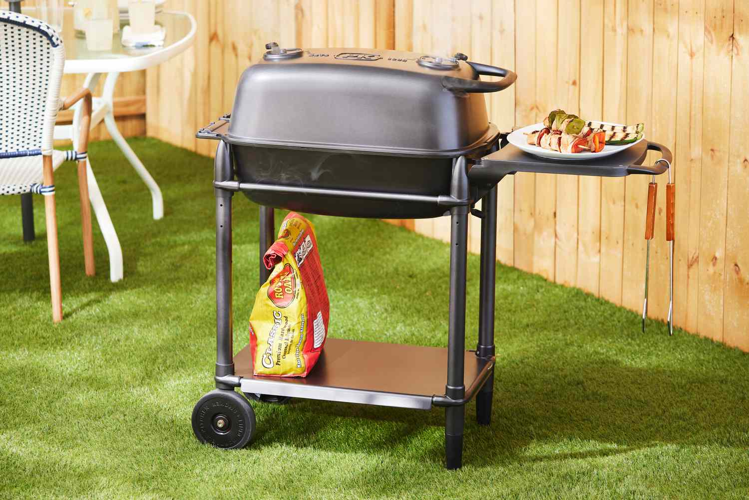 PK Grills PKGo Camp & Tailgate Grilling System in a yard near a fence