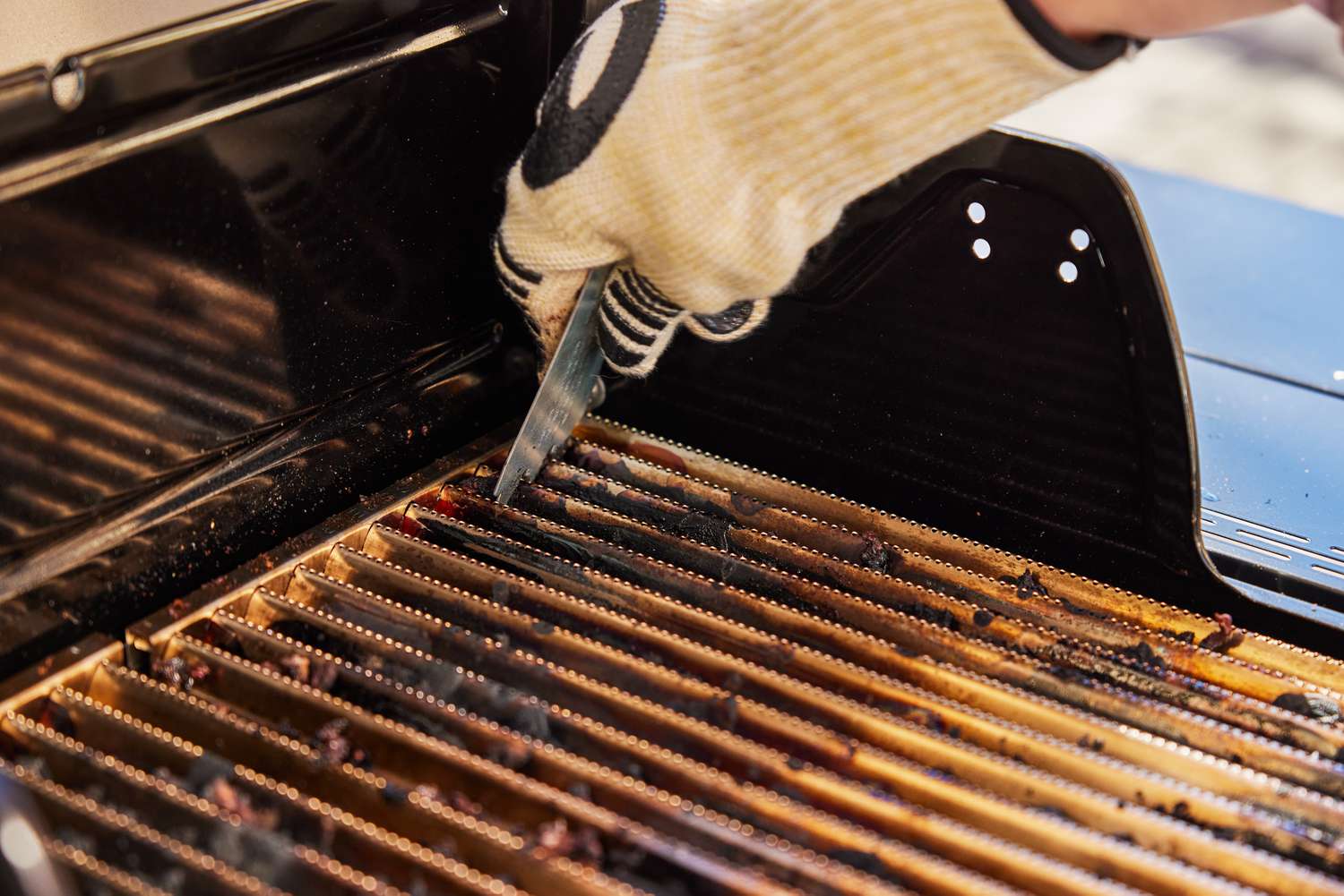 Gloved hand scraping grate of the Char-Broil Signature Series Amplifire 2-Burner Gas Grill