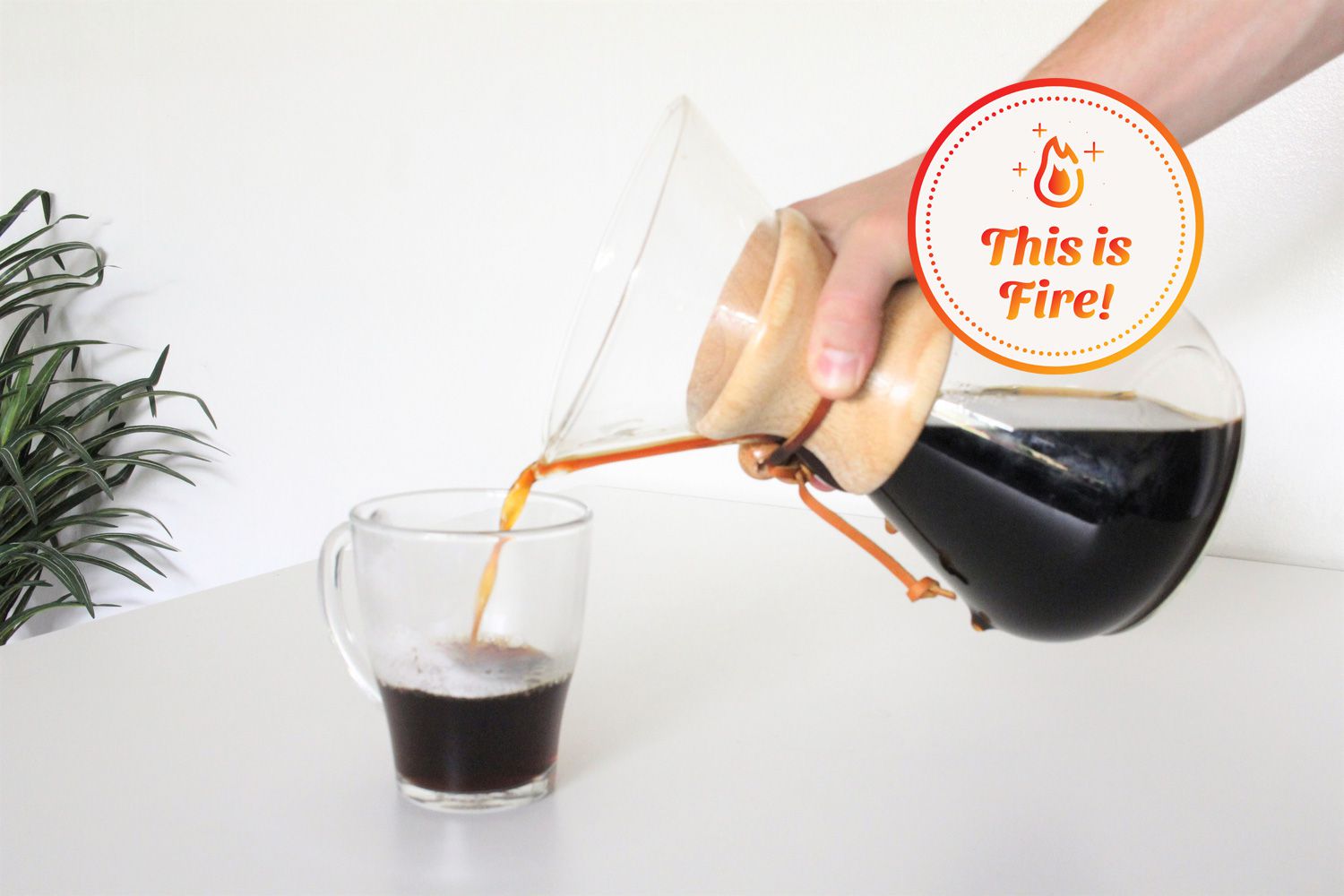 Hand pouring coffee from Chemex Classic Series Coffeemaker into glass coffee mug displayed on white marble countertop