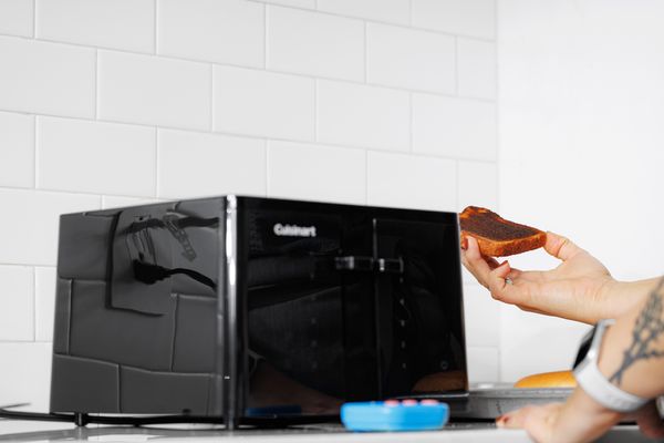 Hand holding a piece of toast next to the Cuisinart CPT-T40 4-Slice Touchscreen Toaster