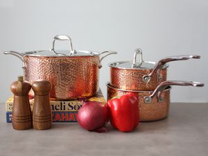 Lagostina Martellata 10-Piece Hammered Copper Cookware Set displayed on a beige surface next to a red pepper and onion